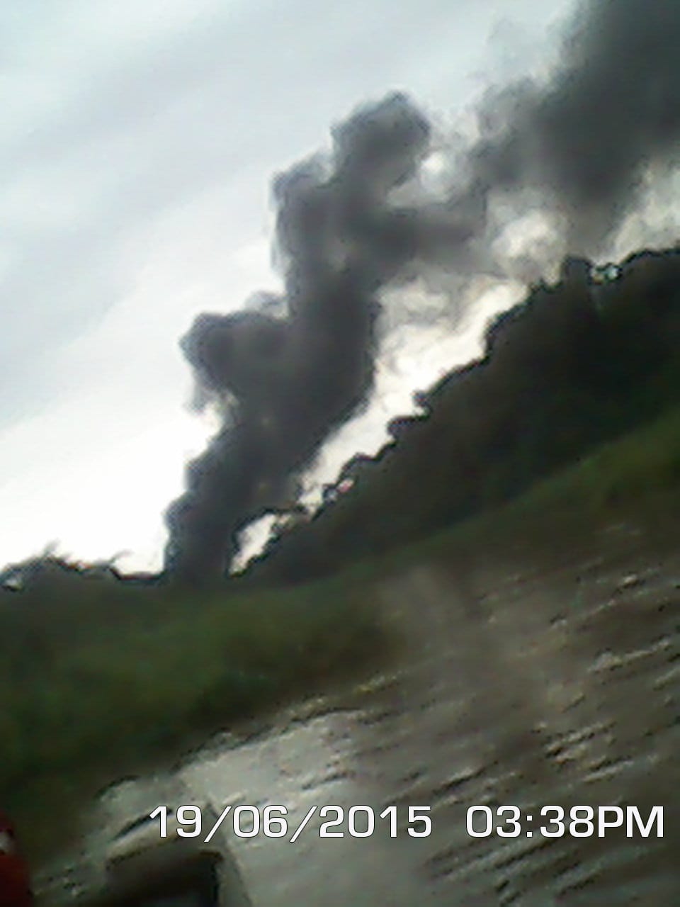 Dark smoke rising above a tree-lined waterway