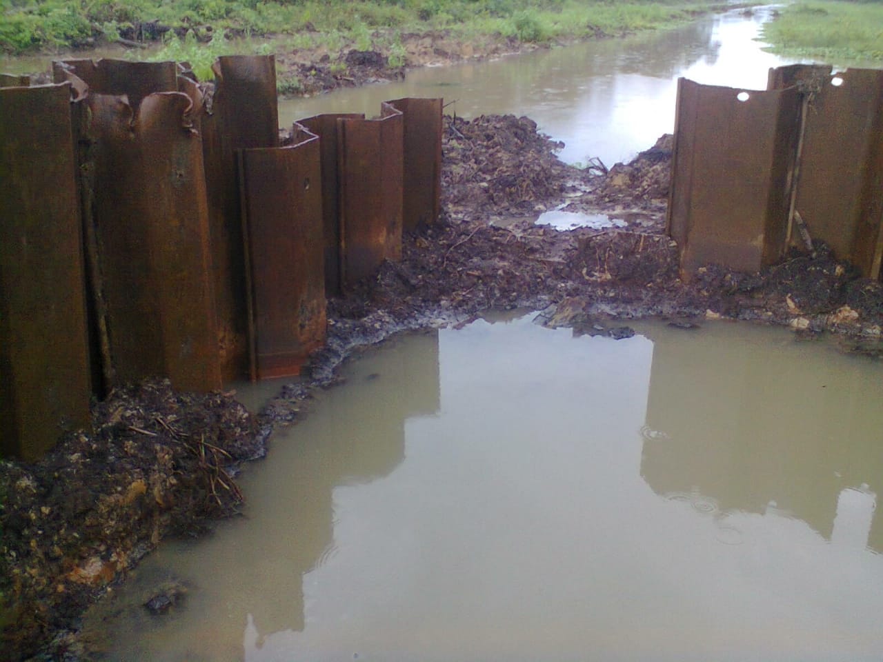 Rusted steel sheet piles forming an enclosure around muddy water